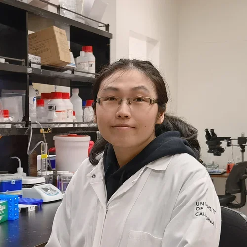 Shanshan Qiao in a lab coat sitting at a lab bench